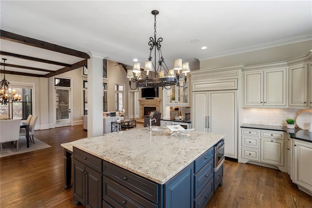 kitchen with a notable chandelier, paneled built in fridge, a kitchen island, a lit fireplace, and dark stone counters