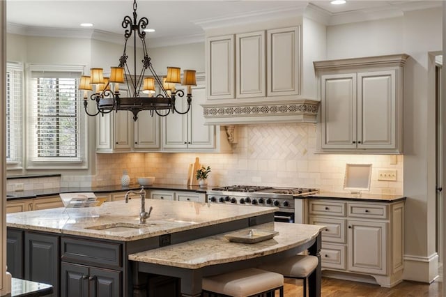 kitchen with premium range hood, a sink, ornamental molding, dark stone counters, and a center island with sink