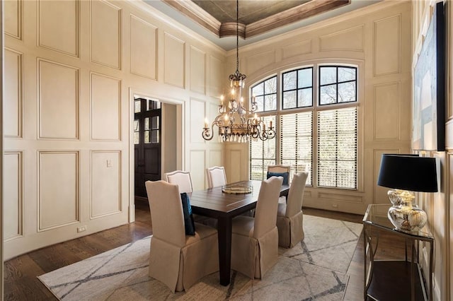 dining space featuring a chandelier, a decorative wall, a high ceiling, wood finished floors, and crown molding