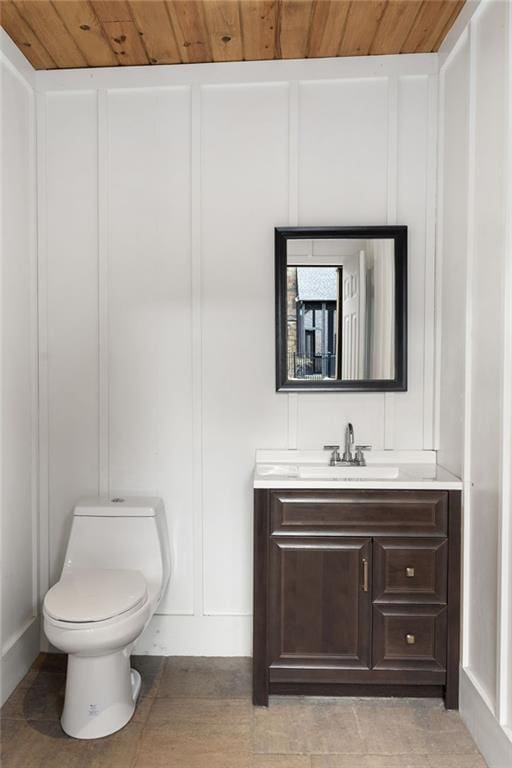 bathroom featuring toilet, wooden ceiling, vanity, and a decorative wall