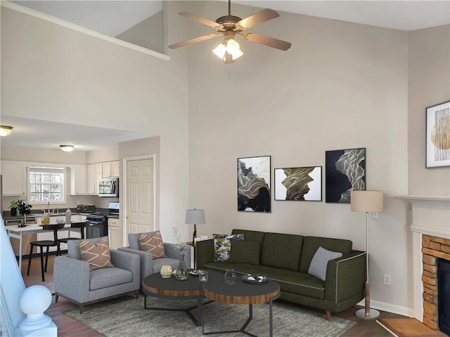 living area featuring baseboards, dark wood finished floors, a stone fireplace, a high ceiling, and a ceiling fan