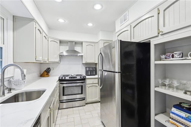 kitchen with visible vents, wall chimney range hood, light stone countertops, appliances with stainless steel finishes, and a sink