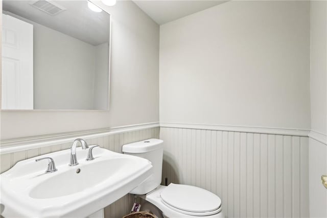 bathroom featuring a sink, visible vents, toilet, and wainscoting