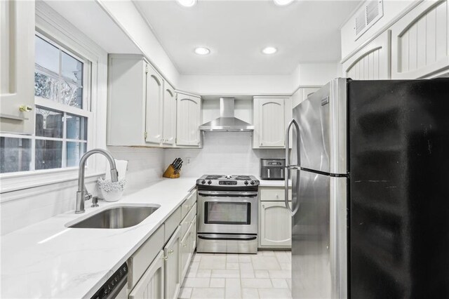 kitchen with visible vents, decorative backsplash, stainless steel appliances, wall chimney exhaust hood, and a sink