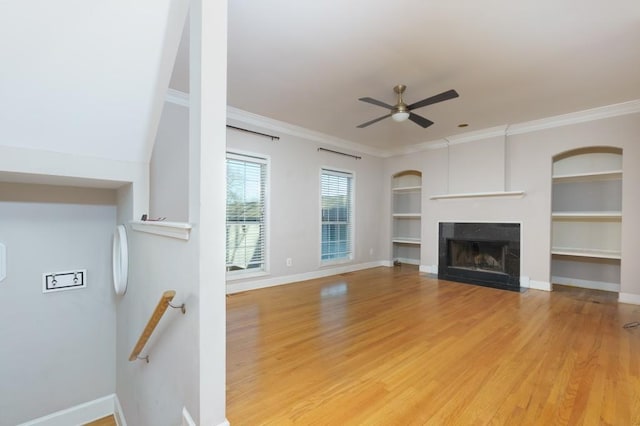 unfurnished living room featuring ceiling fan, built in features, crown molding, and hardwood / wood-style floors