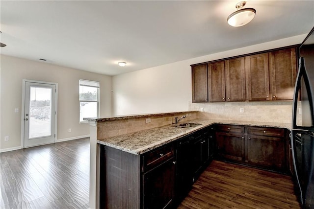 kitchen featuring dark wood-type flooring, sink, light stone counters, black fridge, and kitchen peninsula