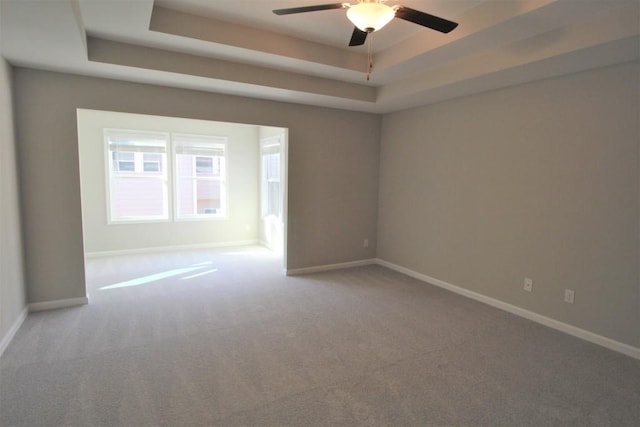 spare room featuring a tray ceiling, baseboards, ceiling fan, and carpet flooring