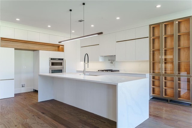 kitchen with appliances with stainless steel finishes, a kitchen island with sink, sink, decorative light fixtures, and white cabinetry