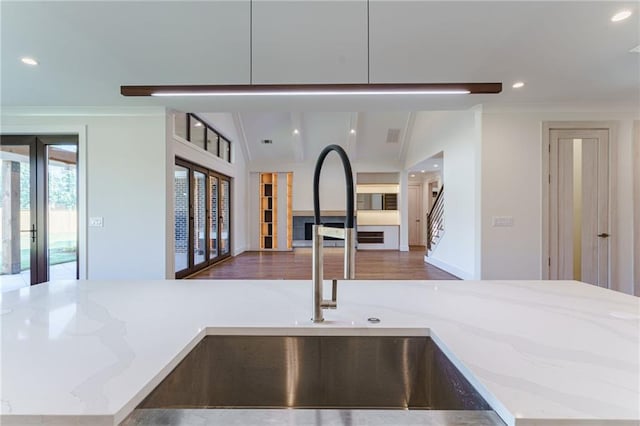 kitchen featuring sink, french doors, light stone counters, crown molding, and hardwood / wood-style floors