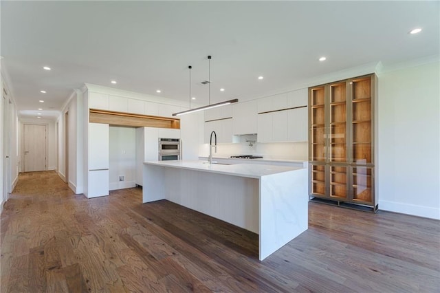 kitchen with sink, dark wood-type flooring, an island with sink, decorative light fixtures, and white cabinets