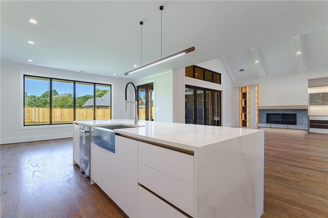 kitchen featuring a kitchen island with sink, a tile fireplace, pendant lighting, dark hardwood / wood-style floors, and white cabinetry