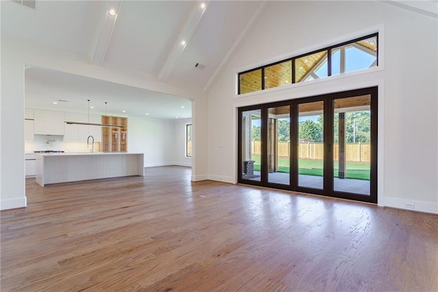 interior space featuring beamed ceiling, light wood-type flooring, high vaulted ceiling, and sink