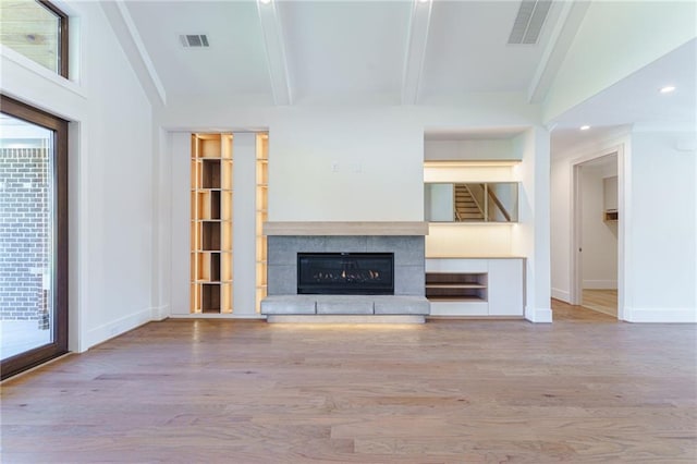 unfurnished living room with beam ceiling, a fireplace, and light hardwood / wood-style flooring