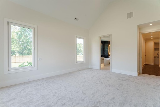 interior space with light carpet, connected bathroom, and high vaulted ceiling