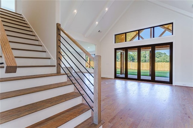 stairs with hardwood / wood-style flooring, beamed ceiling, and high vaulted ceiling