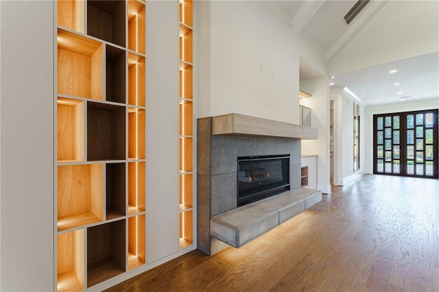 unfurnished living room with french doors, a tile fireplace, hardwood / wood-style flooring, built in features, and vaulted ceiling with beams