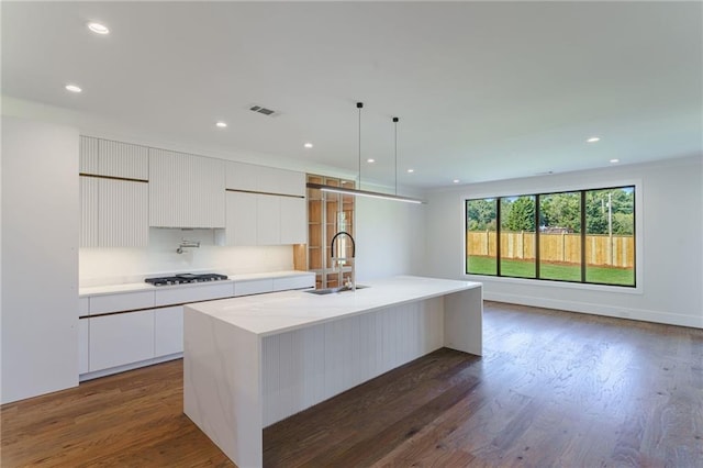 kitchen featuring a center island with sink, white cabinets, hanging light fixtures, and gas cooktop