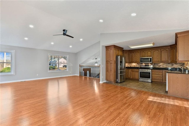 kitchen featuring dark countertops, open floor plan, lofted ceiling, decorative backsplash, and appliances with stainless steel finishes