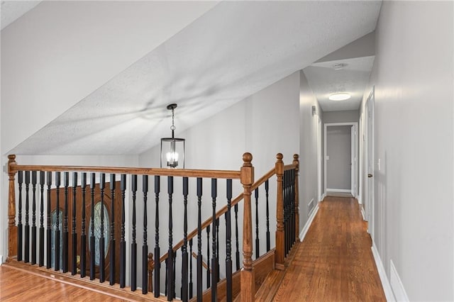 hallway featuring wood finished floors, baseboards, vaulted ceiling, a textured ceiling, and an upstairs landing