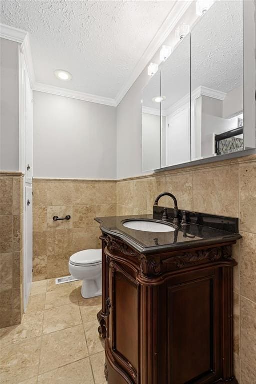 bathroom with toilet, a textured ceiling, tile walls, crown molding, and vanity