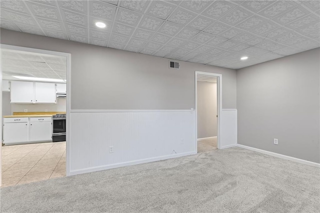 empty room with baseboards, visible vents, recessed lighting, wainscoting, and light carpet