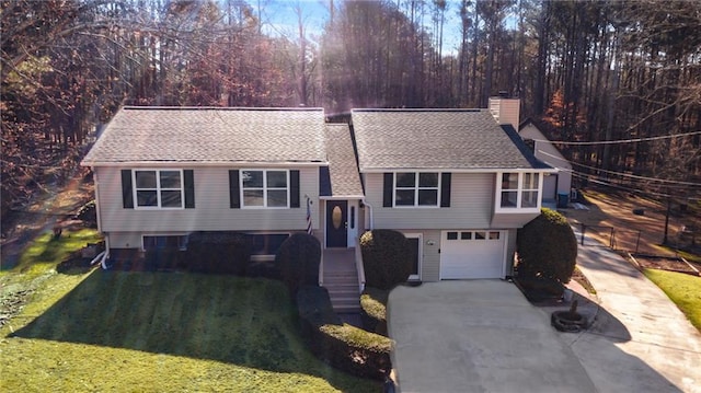 split foyer home with a front lawn, roof with shingles, concrete driveway, an attached garage, and a chimney