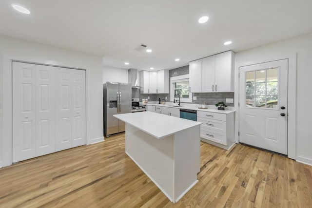 kitchen with wall chimney exhaust hood, sink, appliances with stainless steel finishes, a kitchen island, and white cabinets