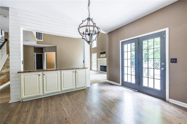 unfurnished dining area featuring baseboards, dark wood-style flooring, a chandelier, stairs, and a fireplace
