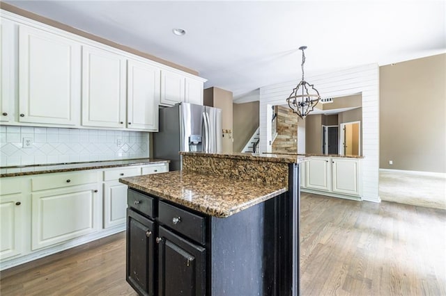 kitchen with stainless steel refrigerator with ice dispenser, a chandelier, light wood-type flooring, backsplash, and a kitchen island