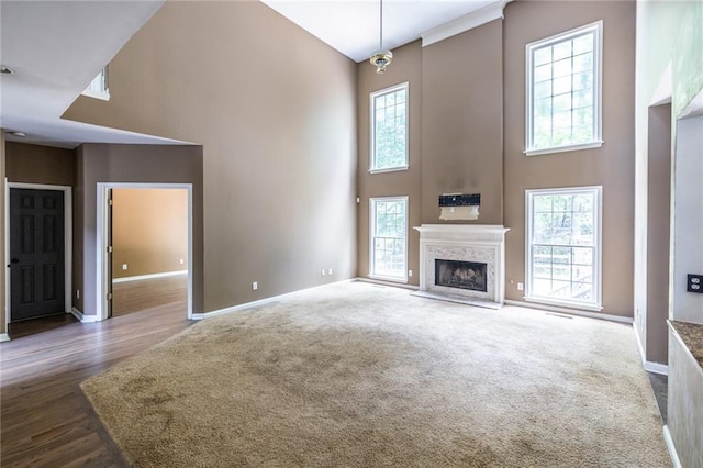unfurnished living room featuring a high ceiling, baseboards, a fireplace with raised hearth, wood finished floors, and carpet floors
