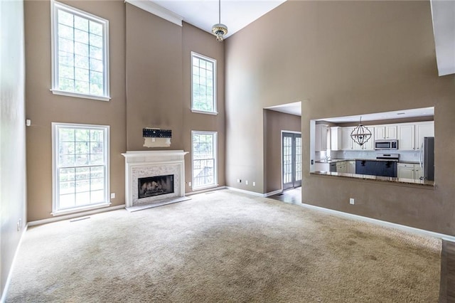 unfurnished living room featuring a towering ceiling, baseboards, a high end fireplace, a chandelier, and light carpet
