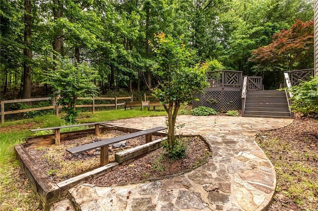view of yard with fence, a patio area, a wooden deck, stairs, and a vegetable garden