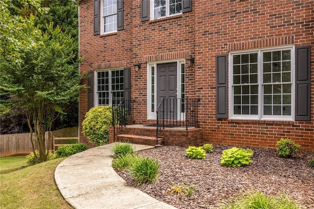 view of exterior entry with fence and brick siding