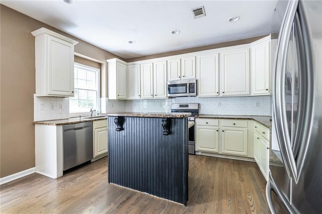 kitchen with appliances with stainless steel finishes, dark wood finished floors, tasteful backsplash, a breakfast bar area, and a kitchen island