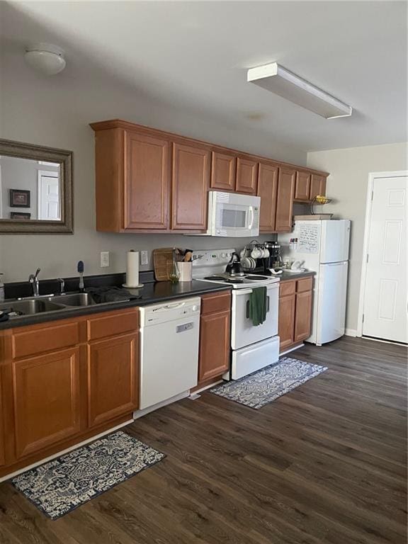 kitchen featuring white appliances, dark wood-type flooring, a sink, brown cabinetry, and dark countertops