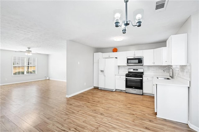 kitchen with white cabinets, ceiling fan with notable chandelier, sink, light hardwood / wood-style floors, and stainless steel appliances