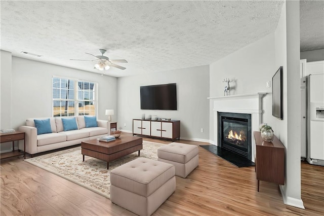 living room with ceiling fan, a textured ceiling, and light wood-type flooring