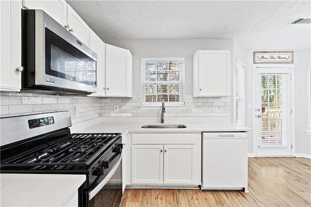 kitchen with white cabinets, sink, light hardwood / wood-style flooring, decorative backsplash, and stainless steel appliances