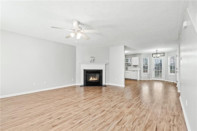 unfurnished living room featuring ceiling fan with notable chandelier, light hardwood / wood-style floors, and a textured ceiling