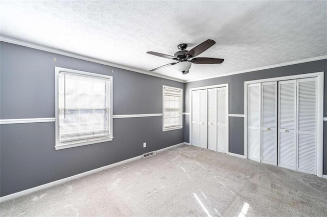 unfurnished bedroom featuring multiple windows, a textured ceiling, two closets, and ceiling fan