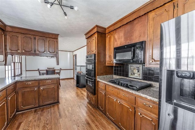 kitchen featuring backsplash, ornamental molding, a textured ceiling, black appliances, and hardwood / wood-style flooring