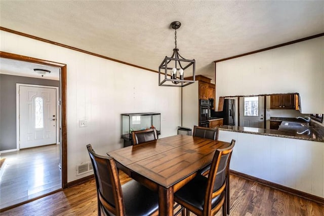 dining space with sink, dark hardwood / wood-style floors, crown molding, a chandelier, and a textured ceiling