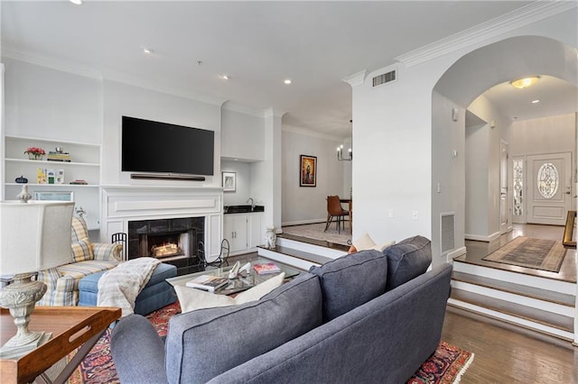 living room featuring wood-type flooring, crown molding, a fireplace, and built in shelves