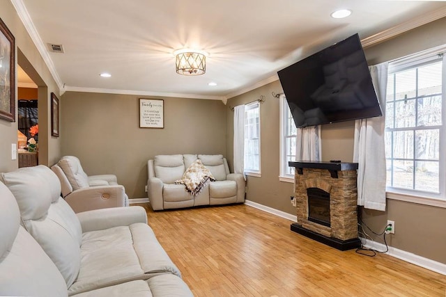 living room featuring a stone fireplace, ornamental molding, light hardwood / wood-style floors, and a healthy amount of sunlight