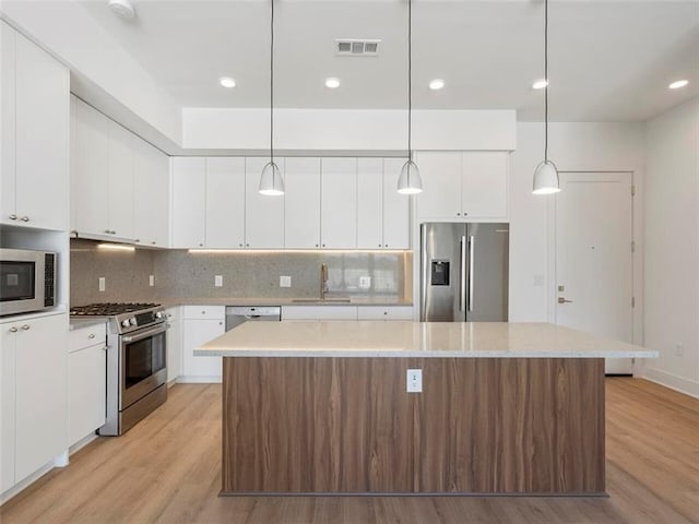 kitchen with hanging light fixtures, light hardwood / wood-style floors, white cabinetry, stainless steel appliances, and sink