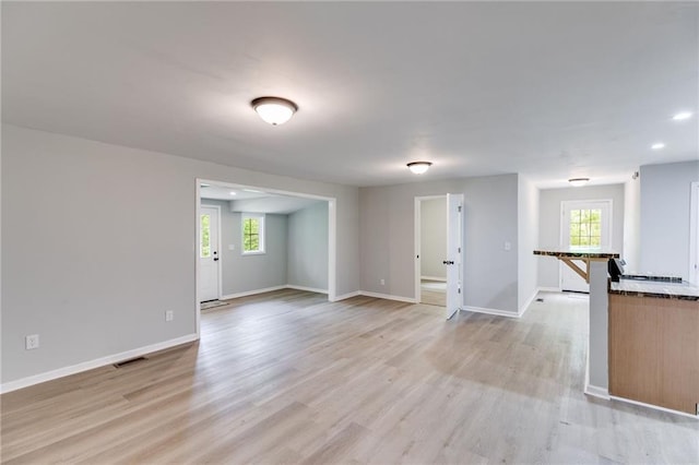 unfurnished living room featuring baseboards, visible vents, light wood finished floors, and plenty of natural light