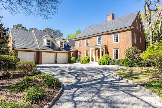 view of front of property featuring brick siding, a chimney, and driveway