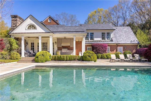 rear view of house with an outdoor pool, a chimney, ceiling fan, a patio area, and brick siding