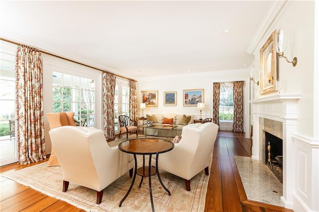 living area with a high end fireplace, hardwood / wood-style flooring, and ornamental molding