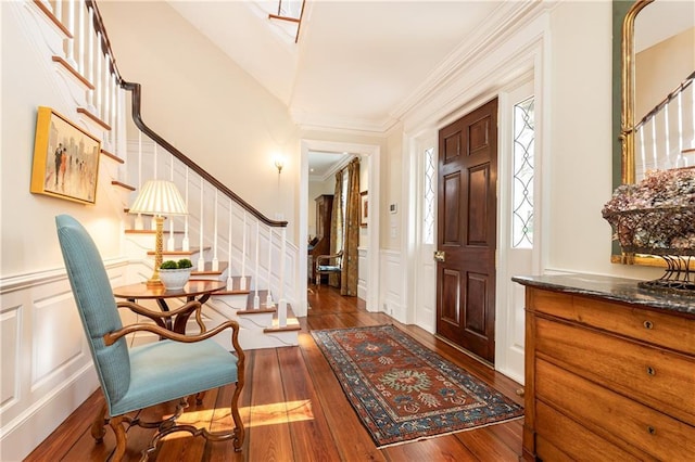 foyer entrance featuring crown molding, stairway, wainscoting, a decorative wall, and wood-type flooring